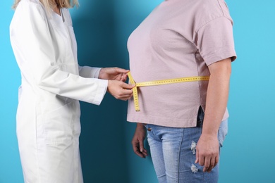 Photo of Doctor measuring fat woman's waist on color background. Weight loss