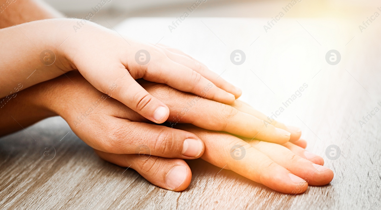 Image of Happy family holding hands at wooden table indoors, closeup. Banner design 