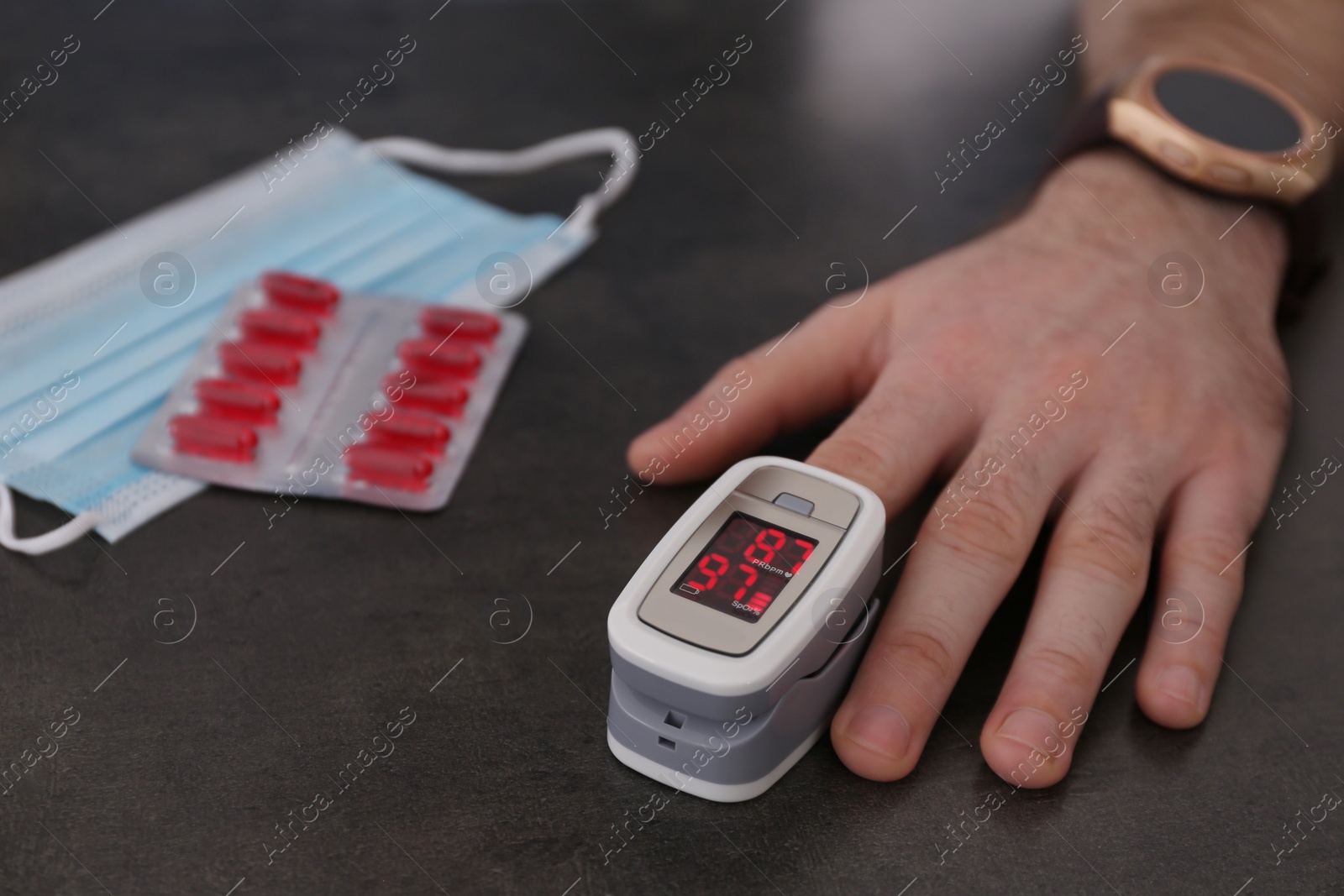 Photo of Man measuring oxygen level with modern fingertip pulse oximeter at grey table, closeup
