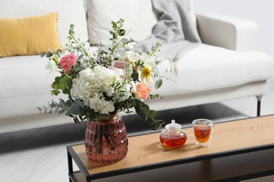 Photo of Bouquet of beautiful flowers and tea on wooden table indoors