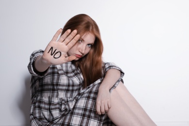 Young woman with word NO written on her palm against light background, focus on hand