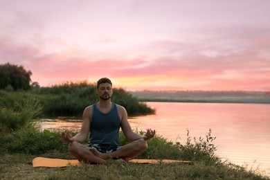 Photo of Man meditating near river in twilight. Space for text