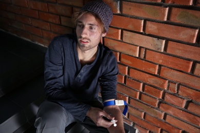 Photo of Male drug addict making injection on stairs near brick wall. Space for text