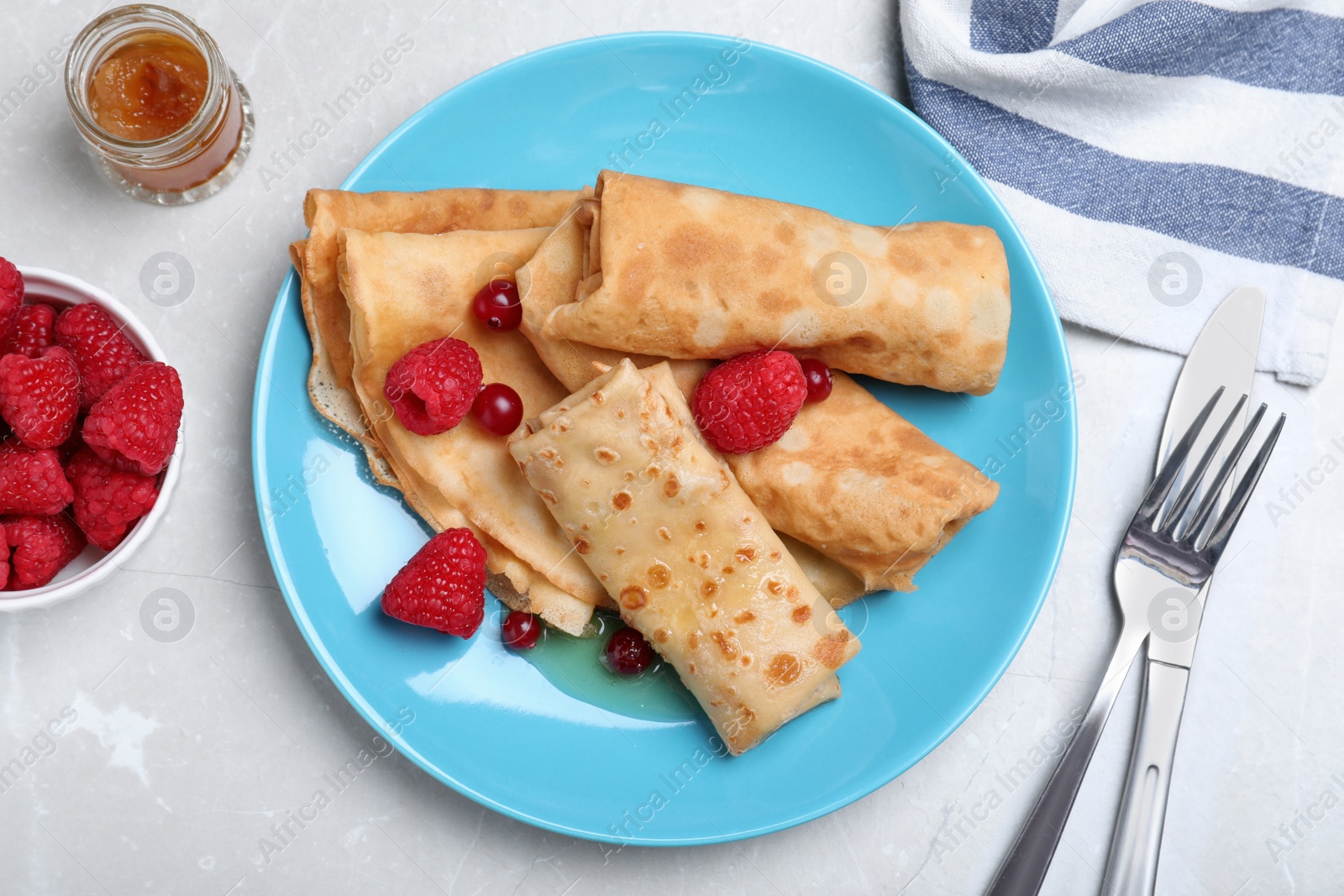 Photo of Delicious crepes served with berries and jam on light grey table, flat lay