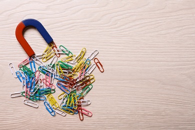 Photo of Magnet attracting colorful paper clips on light wooden background, flat lay. Space for text