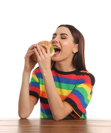 Photo of Young woman eating tasty burger at table on white background