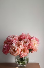 Beautiful pink peonies in vase on table near white wall, space for text