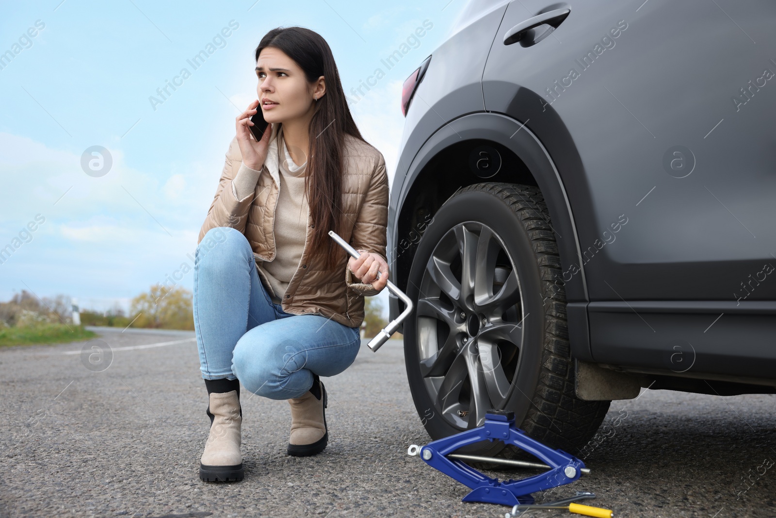 Photo of Worried young woman calling car service. Tire puncture