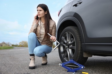 Photo of Worried young woman calling car service. Tire puncture