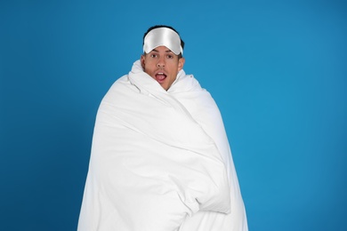 Man wrapped in blanket on blue background