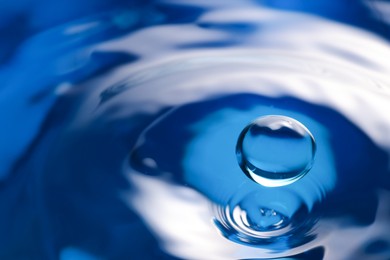 Photo of Drop falling into clear water on blue background, closeup