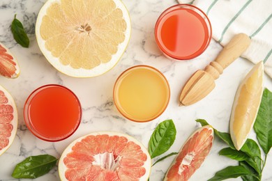 Glasses of different pomelo juices and fruits on white marble table, flat lay