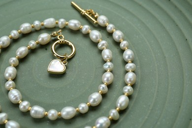 Elegant pearl necklace on olive textured background, closeup