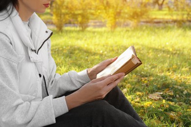 Photo of Woman reading book in park on autumn day, closeup