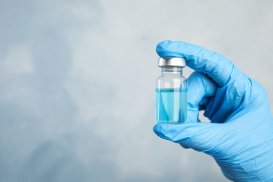 Photo of Doctor holding vial with medication on light blue background, closeup view and space for text. Vaccination and immunization