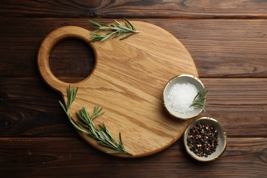 Photo of Cutting board, salt, pepper and rosemary on wooden table, flat lay. Space for text