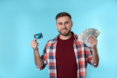 Portrait of happy young man with money and credit card on color background