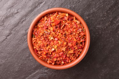 Photo of Chili pepper flakes in bowl on dark textured table, top view