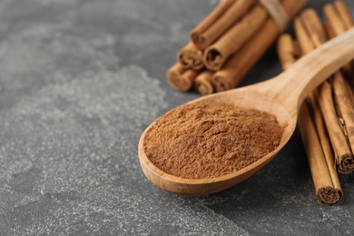 Photo of Aromatic cinnamon powder and sticks on grey table, closeup. Space for text