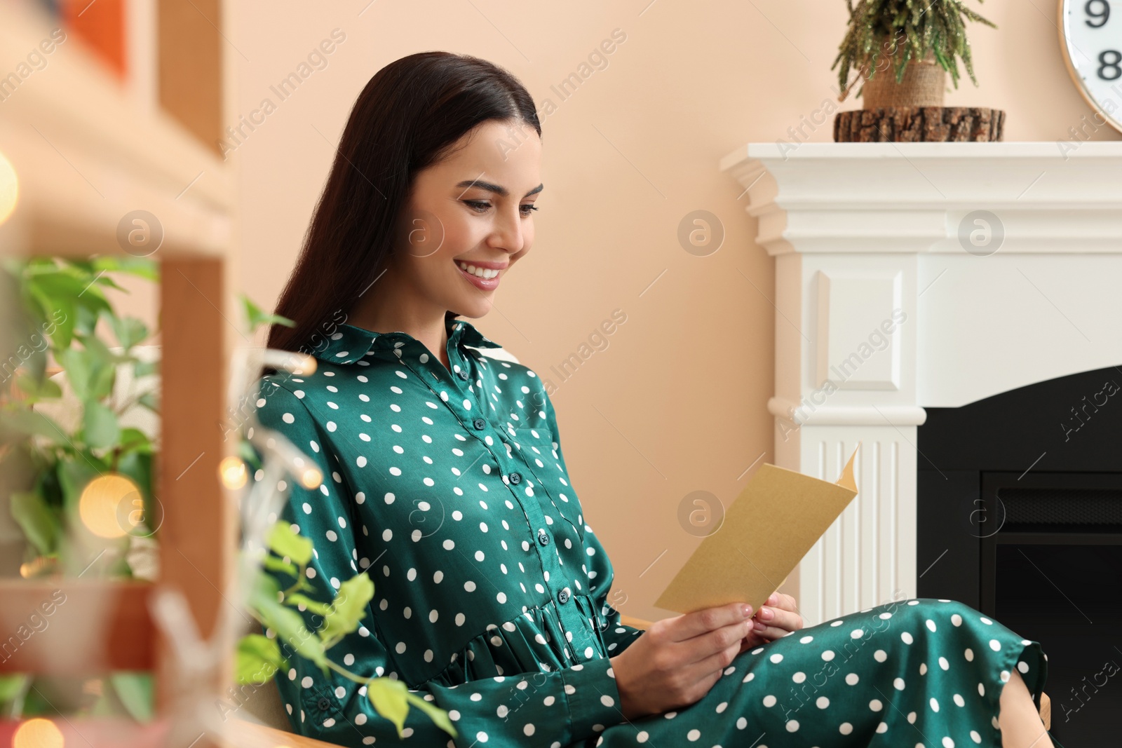 Photo of Happy woman reading Christmas greeting card in living room