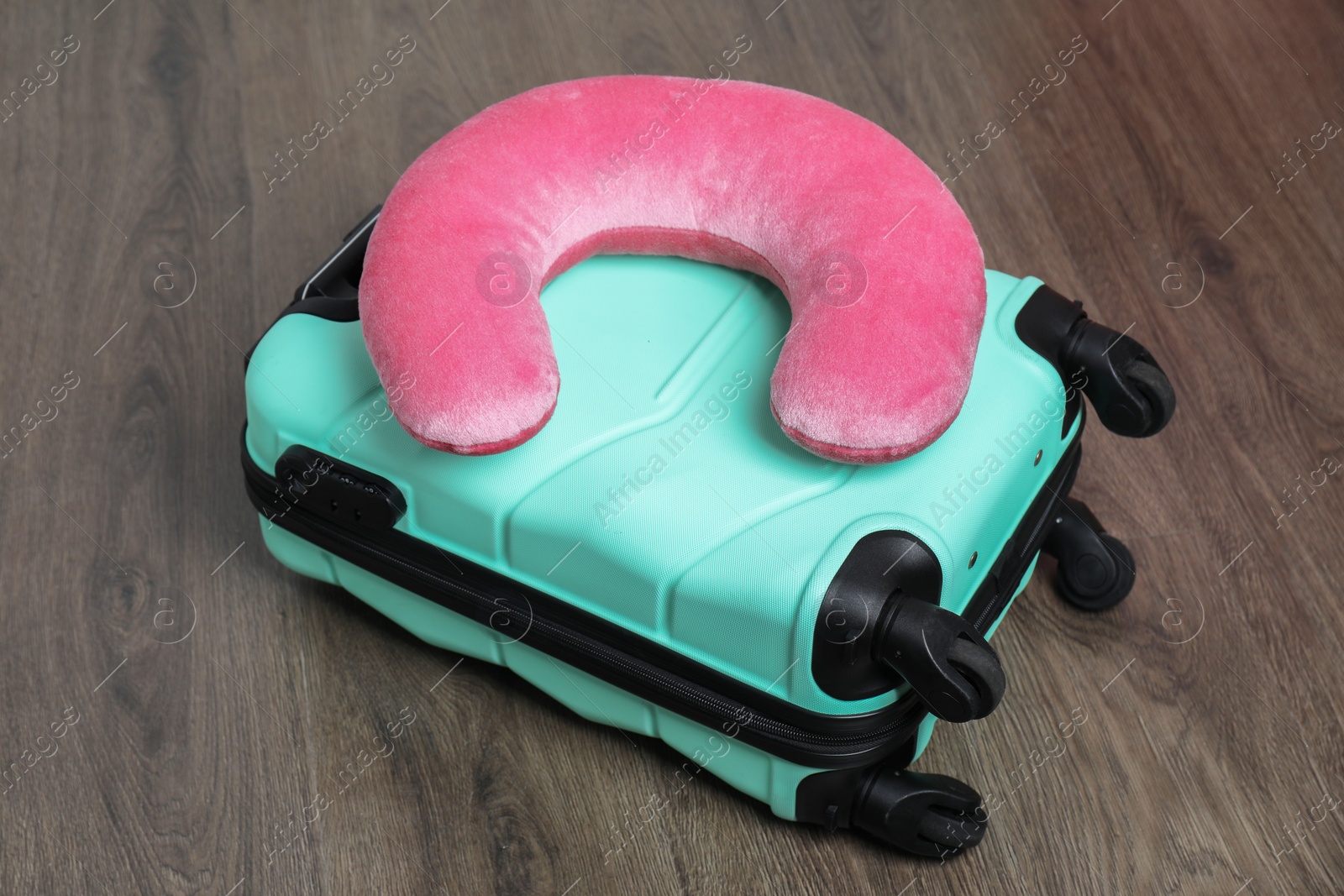 Photo of Pink travel pillow and turquoise suitcase on floor