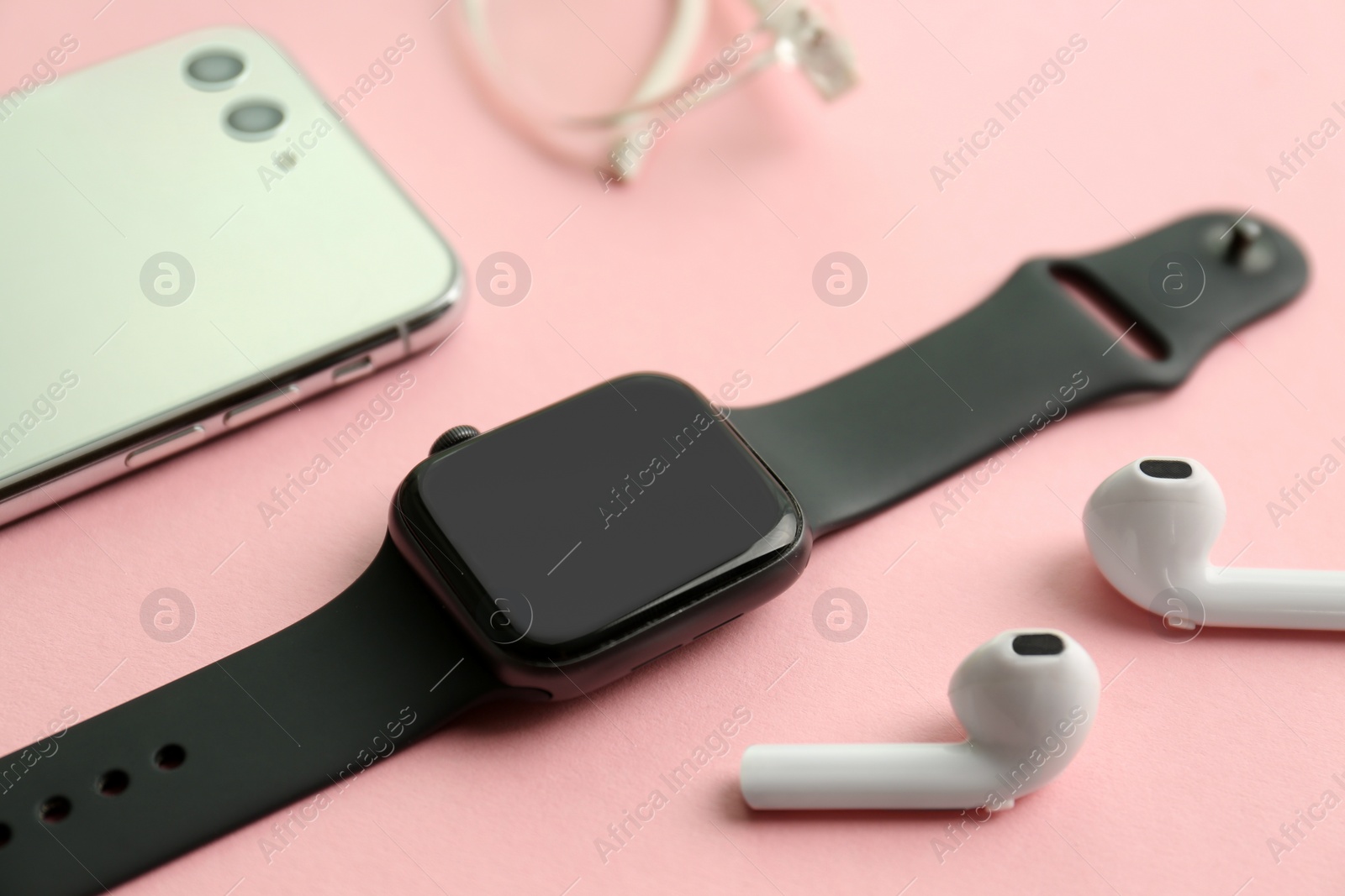 Stylish smart watch, phone and earphones on pink background, closeup Photo of Stylish smart watch, phone and earphones on pink background, closeup