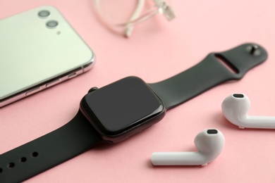 Photo of Stylish smart watch, phone and earphones on pink background, closeup
