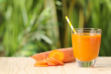 Photo of Glass of tasty juice and fresh carrot on wooden table outdoors. Space for text