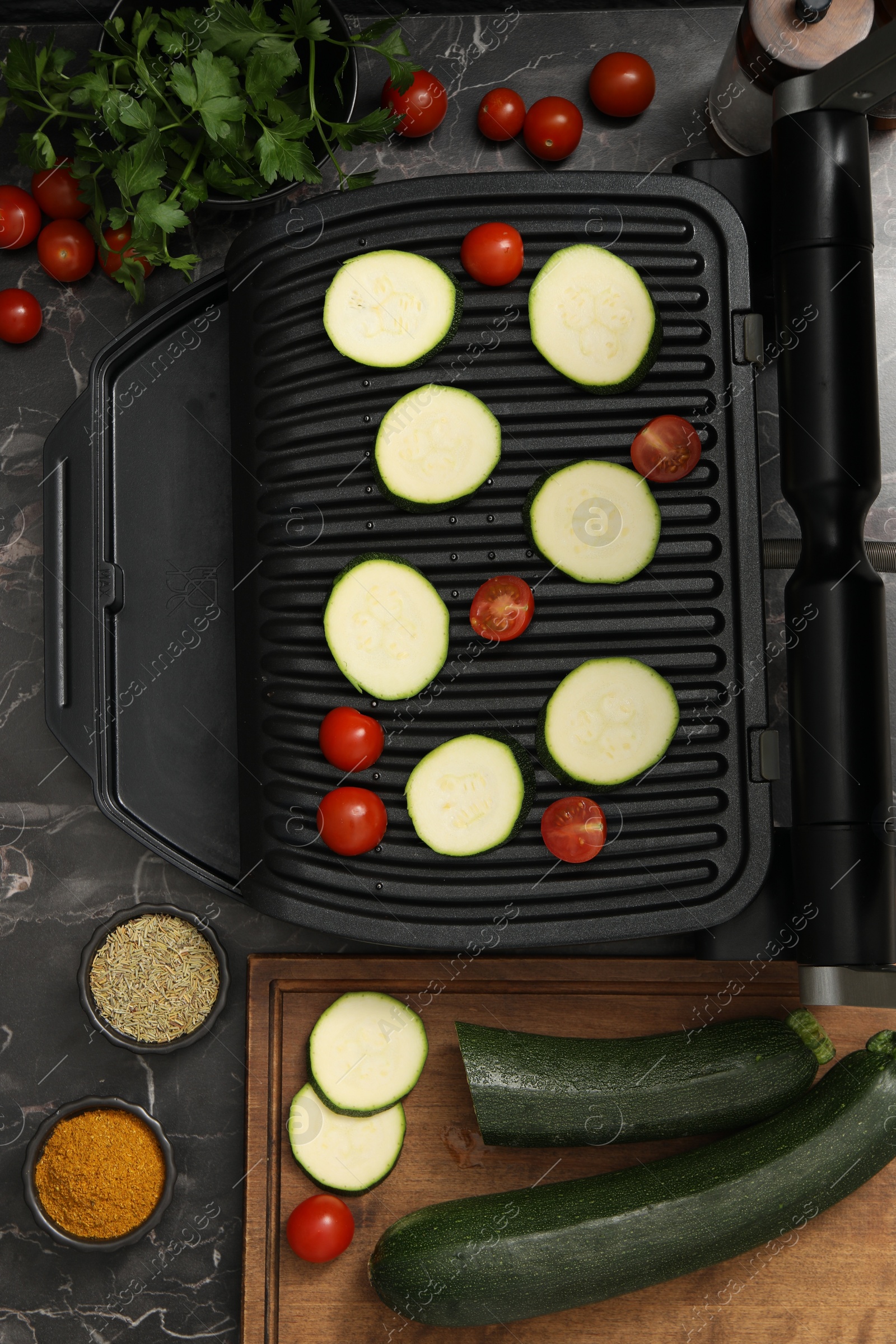 Photo of Electric grill with vegetables and spices on black marble table, flat lay