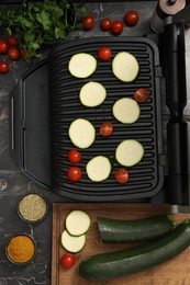 Photo of Electric grill with vegetables and spices on black marble table, flat lay