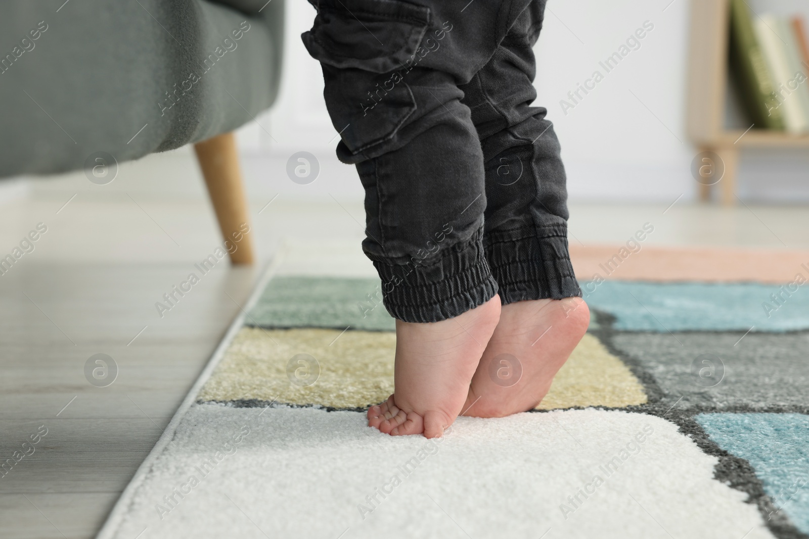 Photo of Baby standing on soft carpet near sofa, closeup