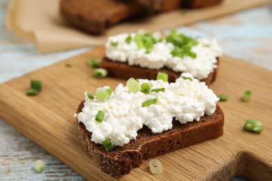 Bread with cottage cheese and green onion on light blue wooden table, closeup