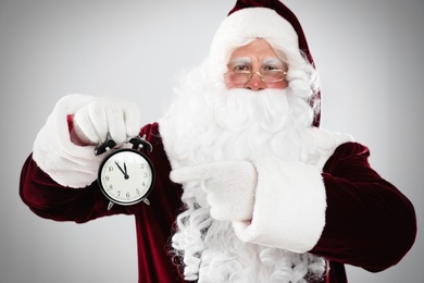 Photo of Santa Claus holding alarm clock on light grey background. Christmas countdown