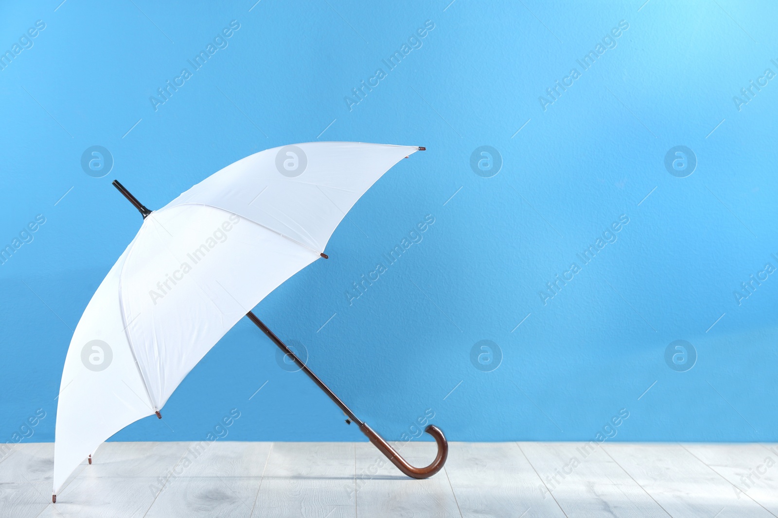 Photo of Beautiful white umbrella near blue wall. Space for text
