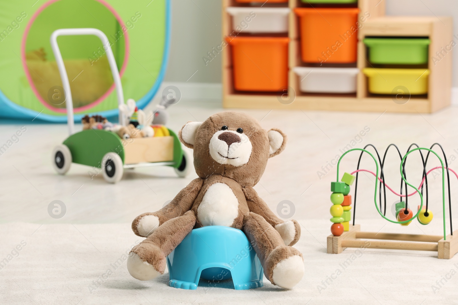 Photo of Cute teddy bear on light blue baby potty on floor in room. Toilet training