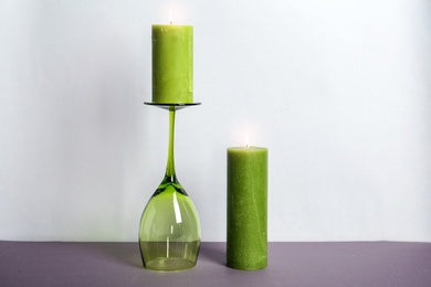 Photo of Decorative wax candles and wineglass on table against light background