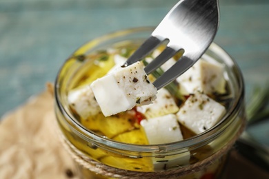 Fork with pickled feta cheese over jar on blue table, closeup