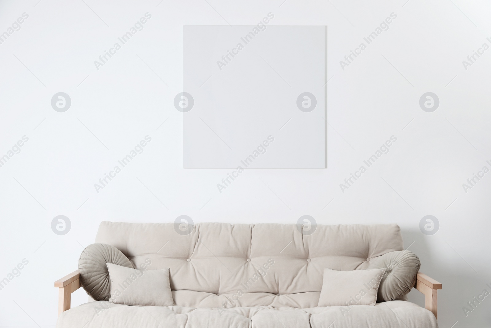 Photo of Blank canvas on wall over beige sofa indoors. Space for design