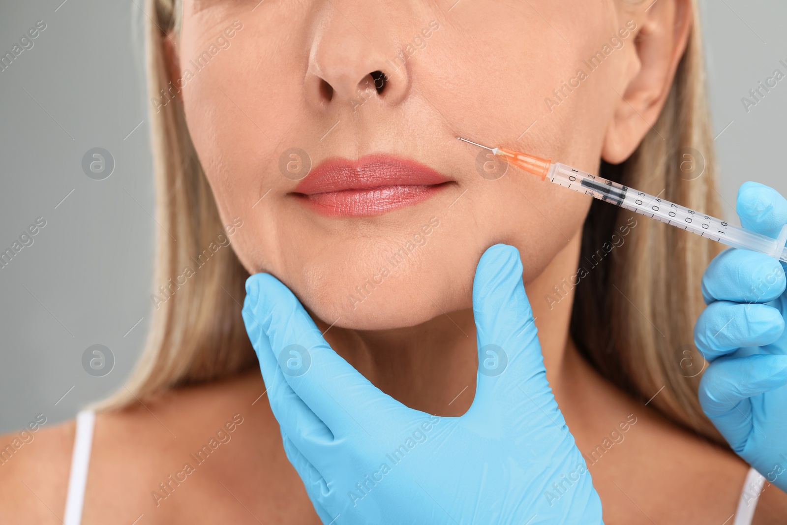 Photo of Doctor giving facial injection to senior woman on light grey background, closeup. Cosmetic surgery