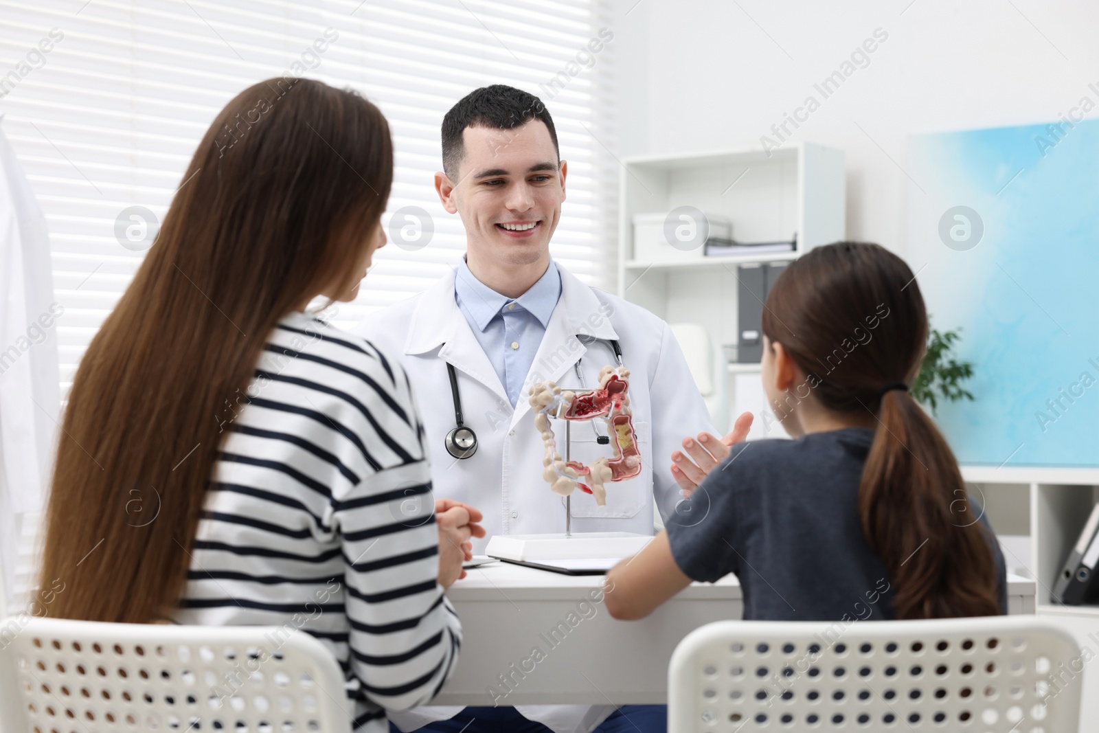 Photo of Gastroenterologist with model of intestine consulting woman and her daughter in clinic