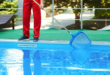 Male worker cleaning outdoor pool with scoop net