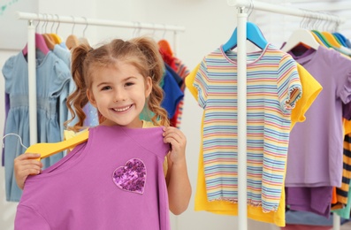 Photo of Little girl choosing clothes on rack indoors