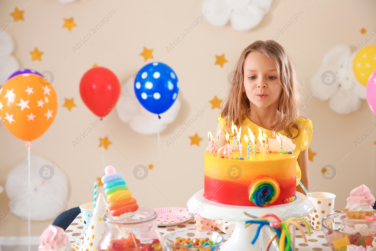 Photo of Cute little girl blowing out candles on her birthday cake indoors