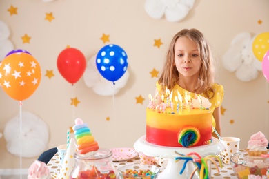 Photo of Cute little girl blowing out candles on her birthday cake indoors