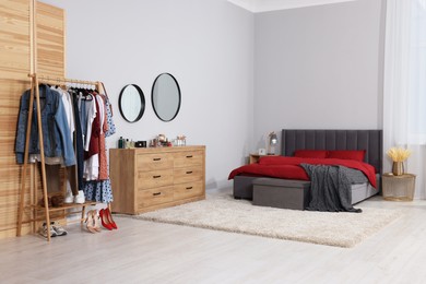 Stylish bedroom with comfortable bed, table, wooden chest of drawers and clothing rack. Interior design