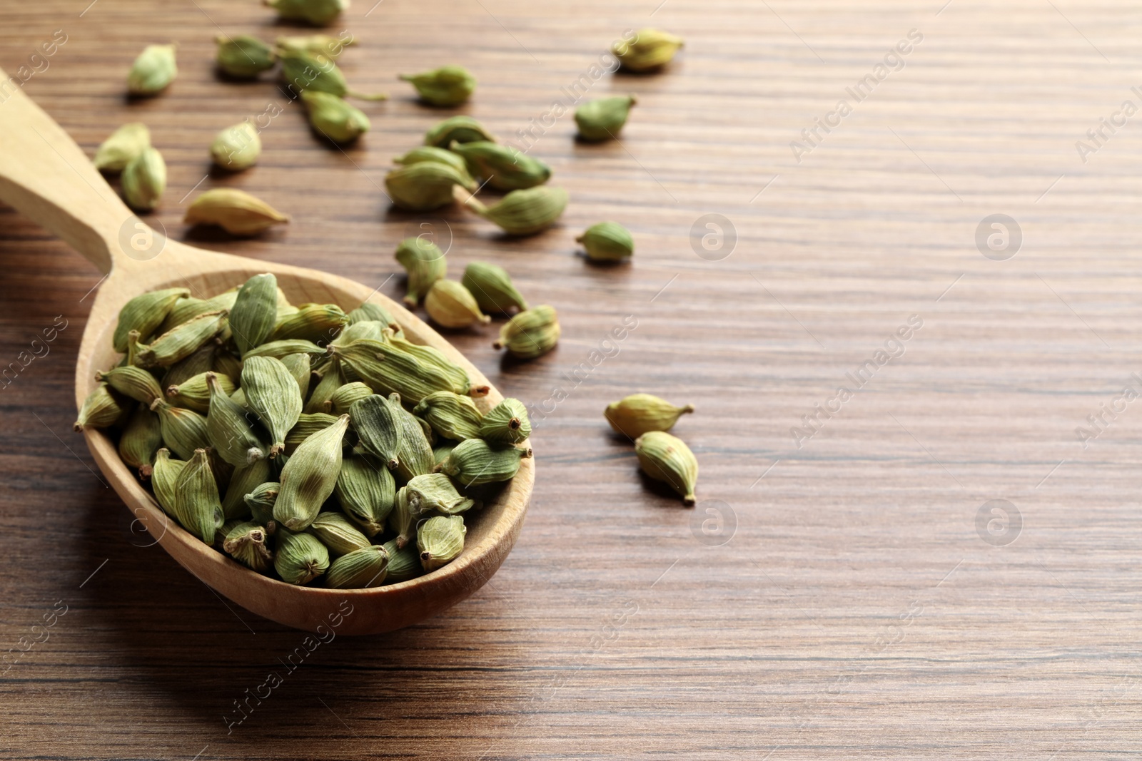 Photo of Spoon with dry cardamom pods on wooden table. Space for text