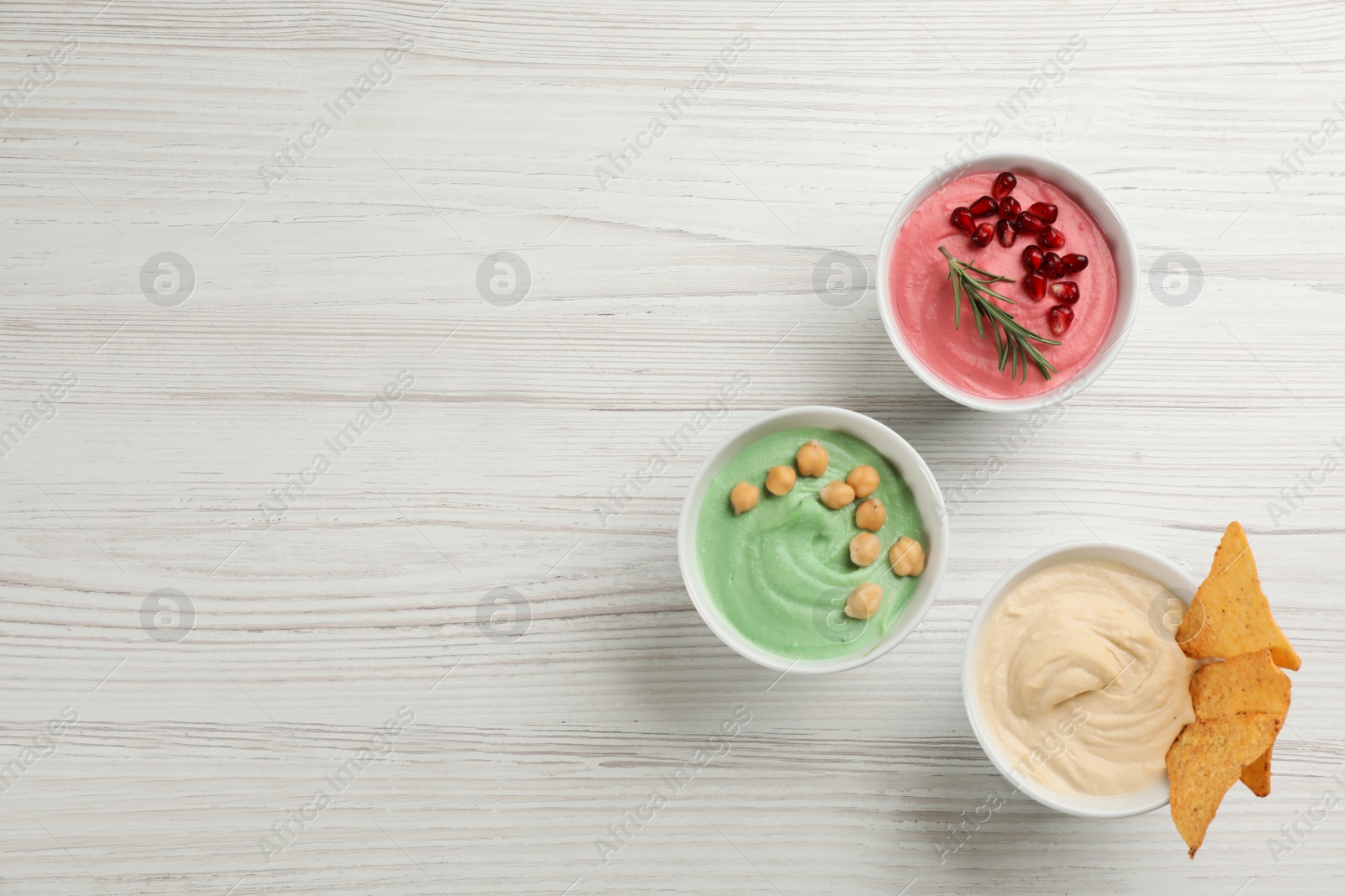 Photo of Different kinds of tasty hummus on white wooden table, flat lay. Space for text