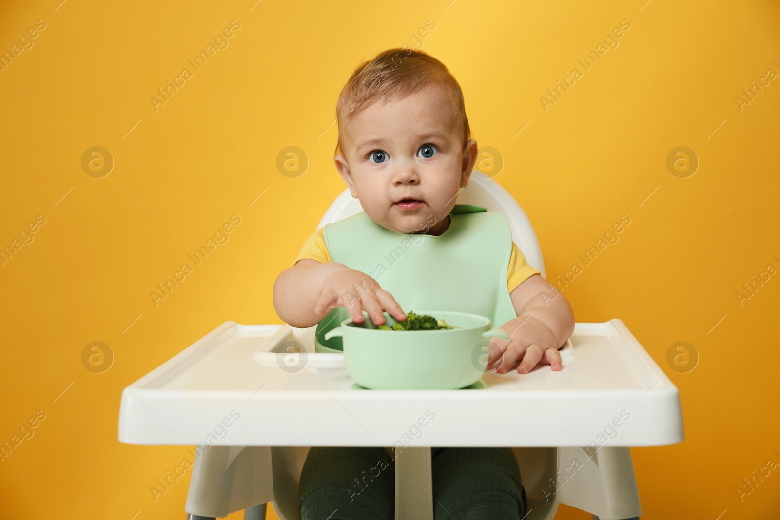 Photo of Cute little baby wearing bib while eating on yellow background