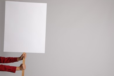 Photo of Woman holding blank sign on light grey background, closeup. Space for design