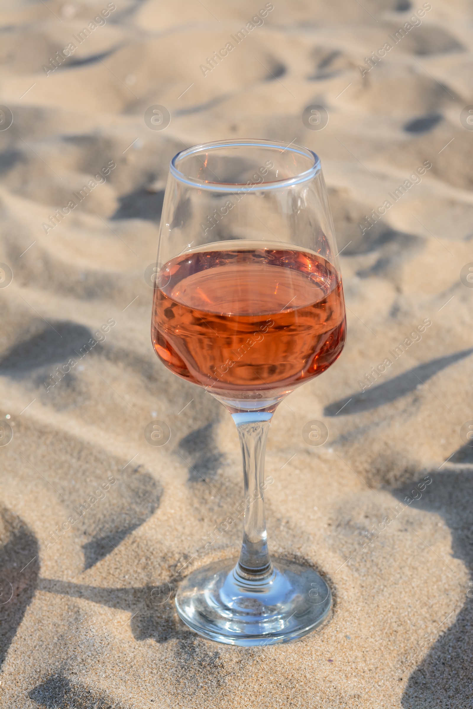 Photo of Glass of tasty rose wine on sand